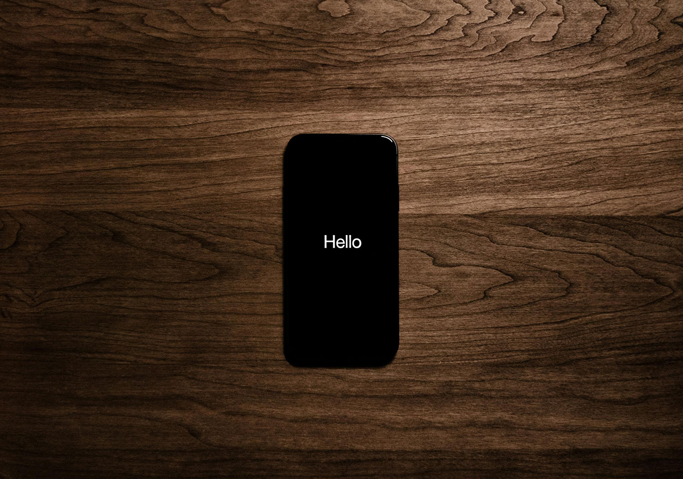 A stark image of a table with a phone in the center. The phone has a black screen except for the words hello to represent how simplicity in marketing can create a stark impact.