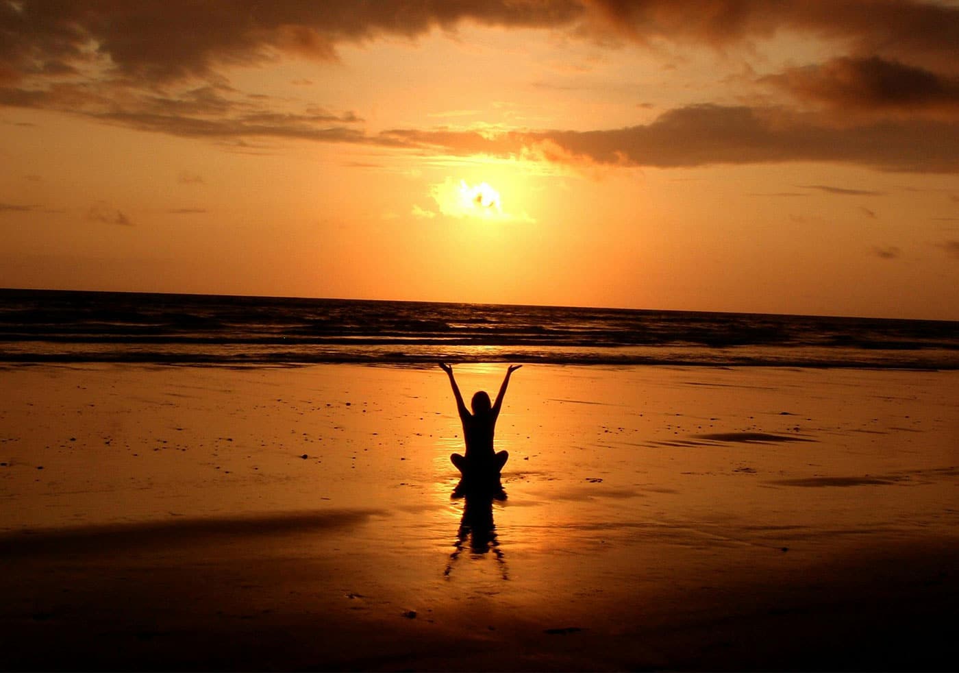 An image of a woman sitting at the beach at sunrise holding her hands up. The image is to represent the beauty of being human and not to forget the human side of marketing decisions and planning.